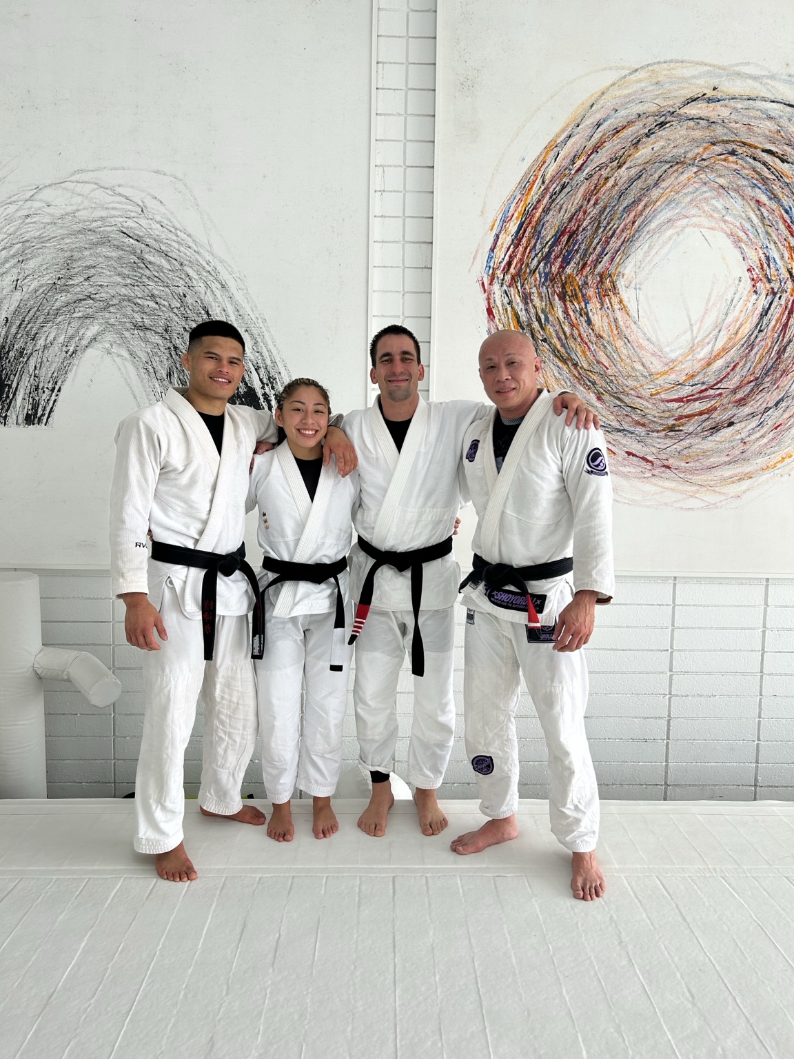 Four jiu-jitsu black belts standing together in white gis on the mat