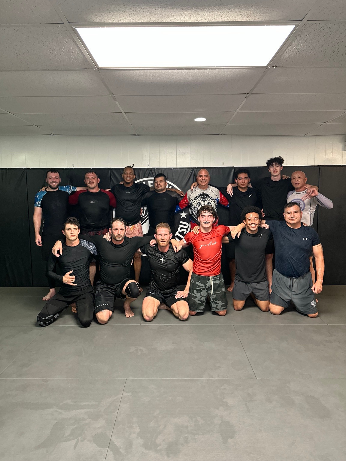 Fourteen academy members in no-gi training clothes gathered together on the mat