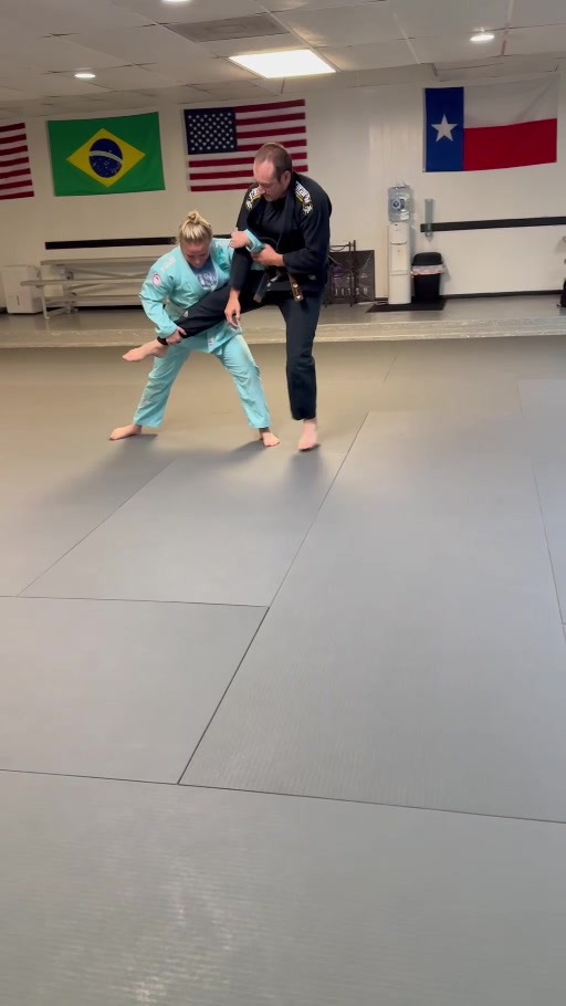 Training partners in turquoise and black gis practicing a standing leg-control drill